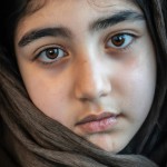 یک دختر نوجوان ایرانی تبار با چشمان قهوه ای با روسری، به حالت عمیق به دوربین خیره شده است.
