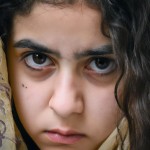 یک دختر نوجوان ایرانی تبار با چشمان قهوه ای با روسری، به حالت عمیق به دوربین خیره شده است.