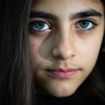 یک دختر نوجوان ایرانی تبار با چشمان قهوه ای بدون روسری، به حالت عمیق به دوربین خیره شده است.