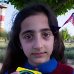 یک دختر نوجوان ایرانی تبار با چشمان قهوه ای بدون روسری، به حالت عمیق به دوربین خیره شده است.بکگراند عکس یک پارک باشه ، بادبادک به دست