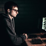 تصویر یک برنامه نویس پشت میز کار در اتاقی تاریک