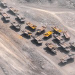 10 number of mining dump trucks located middle of the picture and left and right side is a mountains. the huge truck shovel in middle of them  and cargo and body that resembles like the robots in the Transformers movie