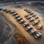 10 number of mining dump trucks located middle of the picture and left and right side is a mountains. the huge truck shovel in middle of them  and cargo and body that resembles like the robots in the Transformers movie