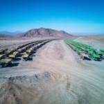 100 number of mining dump trucks located middle of the picture and left and right side is a mountains. the huge truck in middle of them has green lights and cargo and body that resembles like the robots in the Transformers movie