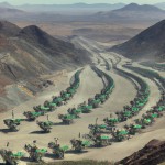 20 lines and 100 number of mining dump trucks located middle of the picture and left and right side is a mountains. the huge truck in middle of them has green lights and cargo and body that resembles like the robots in the Transformers movie