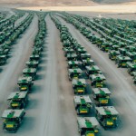 100 number of mining dump trucks located middle of the picture and left and right side is a mountains. the huge truck in middle of them has green lights and cargo and body that resembles like the robots in the Transformers movie