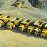 10 number of mining dump trucks located middle of the picture and left and right side is a mountains. the huge truck shovel in middle of them  and cargo and body that resembles like the robots in the Transformers movie