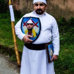 مرد گیلانی با لباس محلی و ریش و سیبل که یک سپر در دست راست خود و یک میزه در دست چپ دارد