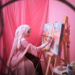 یه دختری زیبا و باحجاب در اتاقش که تم صورتی دارد روی یک بوم نقاشی میکشد