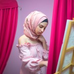 یه دختری زیبا و باحجاب در اتاقش که تم صورتی دارد روی یک بوم نقاشی میکشد