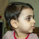 دختری دو ساله با موهای مشکی  کوتاه پسرانه که جلوی موهایش را به طرز ناشیانه ای خودش کوتاه کرده و رنگ پوستش گندمی است با چشمانی فندقی و بینی و لبانی کوچک و چشمانی سیاه ک