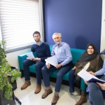سه نفر آقای میانسال،دو نفر آقای جوان ، یک خاتم مسن و یک خانم منشی جوان در اتاق  انتظار نشسته و منتظر مدیر می باشند، محیط کار ایرانی،  فضای روشن. با یک پنجره رو به باغ پاییزی . دو نفر آقا با پیراهن های آبی رنگ مدارکی در دست دارند.