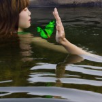 Photo of Taehyung in the water with a green dress and a butterfly on his hand in the water