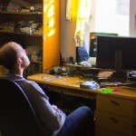A crowded room and an old computer on the table, a window with light coming from outside, warm lighting, a 30-year-old man with white hair sitting on a chair and thinking about upgrading everything