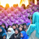 تصویر یک دختر محجبه ی عکاس که در یک جلسه بزرگ در حال عکاسی است