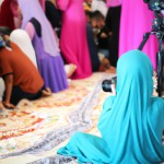 تصویر یک دختر محجبه ی عکاس که در یک جلسه بزرگ در حال عکاسی است