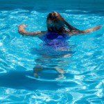 یک دختر جوان با موهای بلند در حال شنا در استخر خصوصی