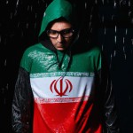 تصویر یک مرد جوان که در حال قدم زدن در باران است و هودی بر تن دارد و کلاه هودی روی سرش است و تصویر روی هودی تصویر پرچم ایران است