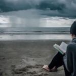 آدمی کنار ساحل با کتاب عاشقانه وهوای بارانی