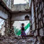تصویر یک کودک که لباسی به رنگ پرچم فلسطین دارد و در یک خانه خراب شده در حال بازی کردن است
