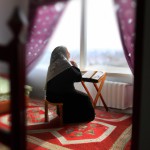 یک خانم پیر که بر سر سجاده نماز مشغول عبادت میباشد و رحل قرآن روبروی آن باز است و آفتاب از پنجره به اتاق میتابد
