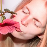 یک دختر بچه کوچک مو زرد در حال بو کردن یک گل صورتی