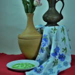 یک کوزه سفالی سنتی ، یک ظرف غذا خوری چوبی سنتی و یک سفره سنتی در کنار یک گلدان گل سنتی به همراه شعری از حافظ
