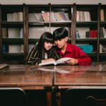 دختر و پسر نوجوان علاقمند به کتاب، در حال کتاب خواندن در کتابخانه بزرگ پشت میز مطالعه.