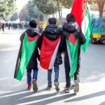 سه پسر 12 ساله ایرانی و عراقی و فلسطینی با پرچم های ایران و عراق و فلسطین بر دوش در حال حرکت به سمت حرم امام حسین در مسیر پیاده روی اربعین