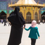 کودکی که دست در دست مادر روبه روی حرم امام رضا ایستاده است