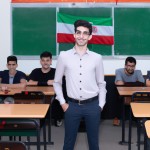 بیست دانش آموزپسر ایرانی که کلاس نهم هستند و در کلاس مطالعات اجتماعی هستند و پیراهن سورمه ای و شلوار مشکی پوشیدن و خیلی خوش تیپ هستند و فضای کلاس هم خیلی زیباست و پرچم ایران پشت سرشون هست.