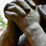 It shows two stone hands clasped together and praying