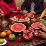 خانواده ایرانی پشت میز در شب یلدا با هندون و انار روی میز