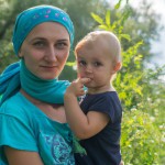 یک مادر با چادر و بجه یک ساله در  آغوش  که اطراف آن سبزی و چمن باشد