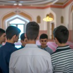 A friendly group of teenage Muslim boys in a mosque looking towards an unidentified person in the picture, from a rear angle.