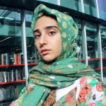 تصویر دختر زیبا و محجبه با چشم و آبروی مشکی و رنگ صورت سبزه، دختر ۲۰ ساله است و کنار مغازه کتابفروشی ایستاده، پیراهن بلند چین دار گلدار تنش است، و حجابش را هم با روسری سبز کامل کرده