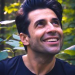 عکس از خاننده معروف ایرانی حامیم درحال لبخند زدن و چشم هایی که از عشق پر شده و عاشق است در یک جنگل و در حالی که یکم سرش رو کج کرده
