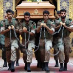 ۴ شهید قوی با لباس پوشیده سپاه ایران در حال هل دادن  تابوت چوبی به وسیله زنجیر بر روی زمین