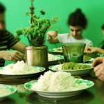 A photo of an Iranian family sitting at the lunch table, busy with their Iranian rice, with a green color theme.