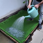 فردی با یک آب‌پاش بزرگ و پر از آب، با دقت و وسواس در حال آب دادن به یک تکه چمن بسیار کوچک و مصنوعی در حیاط خانه‌اش است. آب از اطراف چمن مصنوعی سرازیر شده و به پیاده‌روی سیمانی می‌ریزد و به فاضلاب می‌رود.