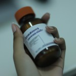 عکس دست یک دختر ک  شیشه دارو در دستش است و روی دارو اسم و مشخصات دارو نوشته شده است