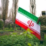 عکس سربازی در باغ که پرچم ایران به دست دارد